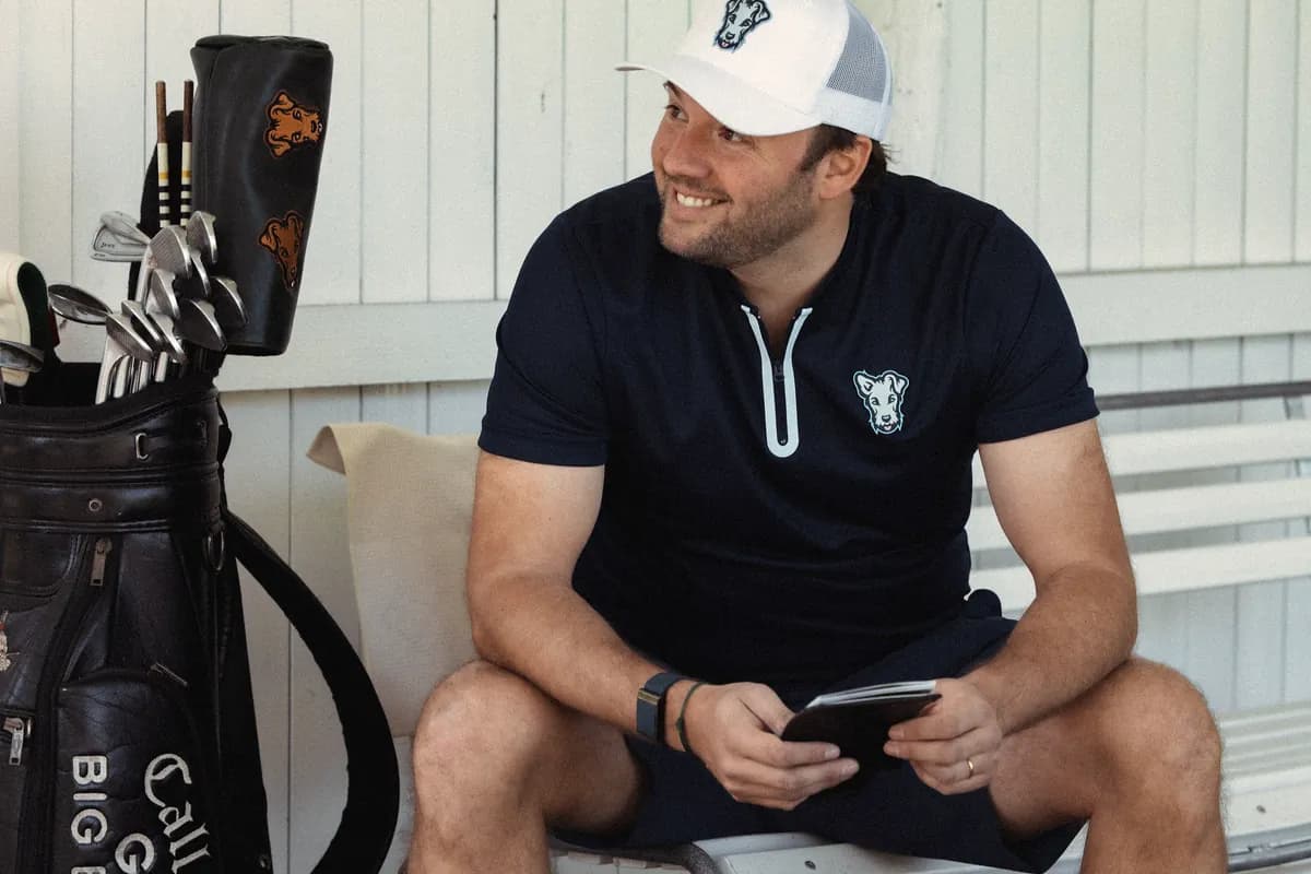 Golfista sentado en la casa club, con el móvil en la mano, junto a su bolsa