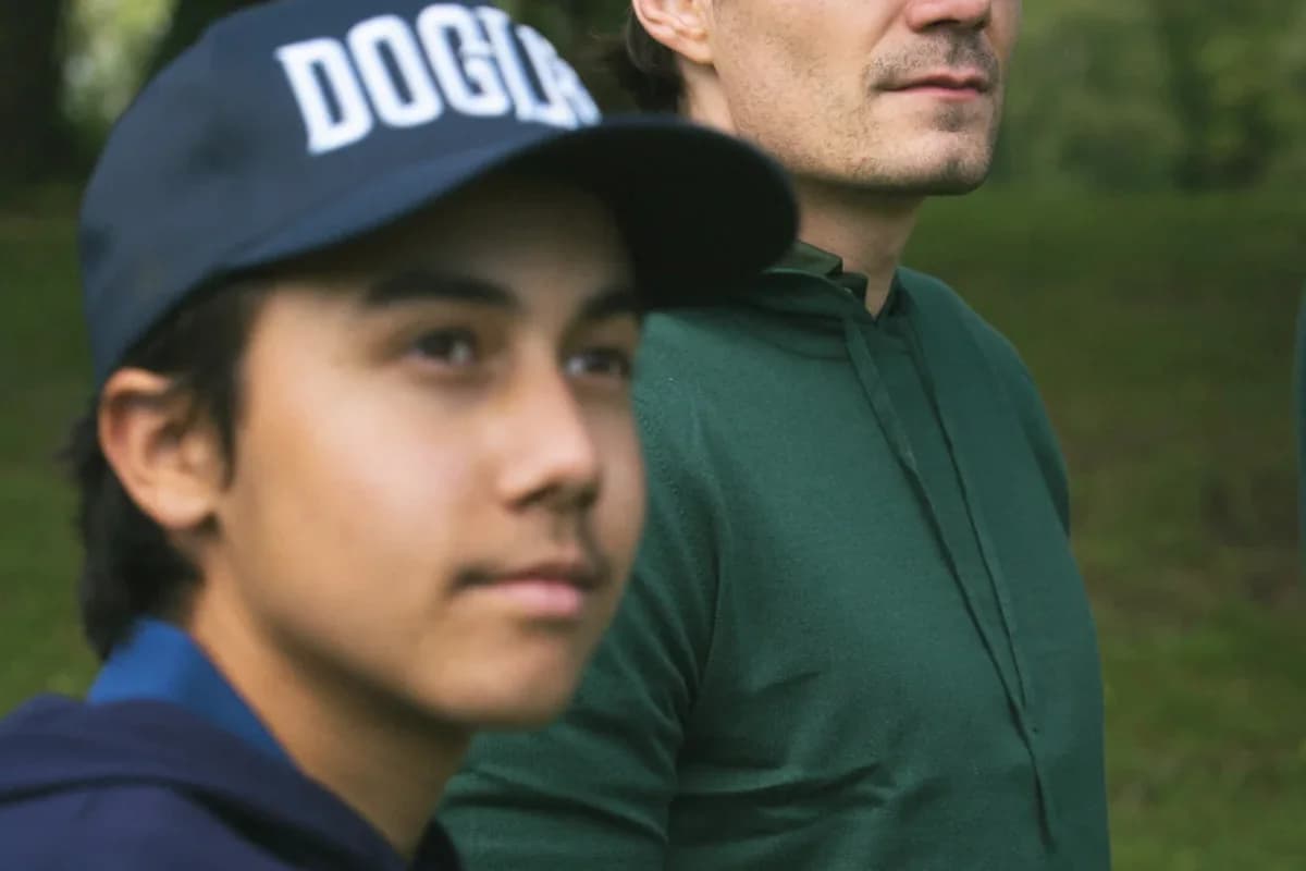Een volwassene en een jonge golfer op de baan, cap en groen breigoed