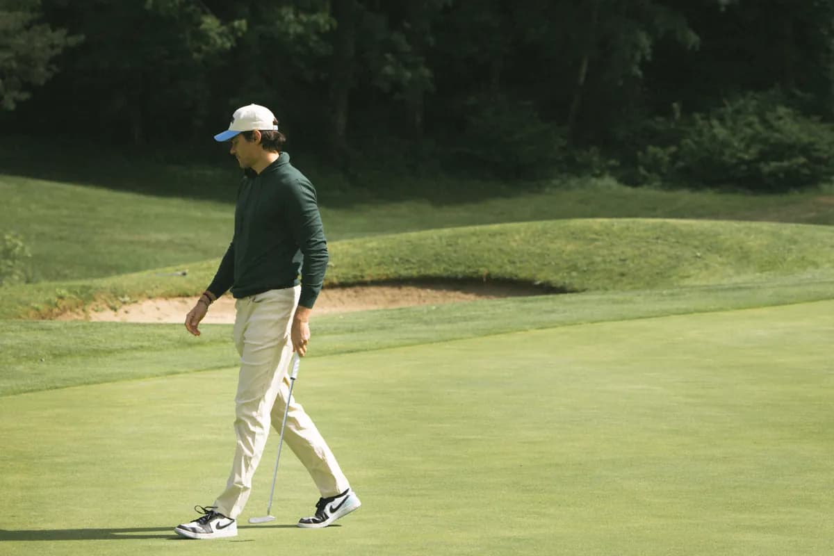 Golfer in a green cardigan walking on the green, near a bunker