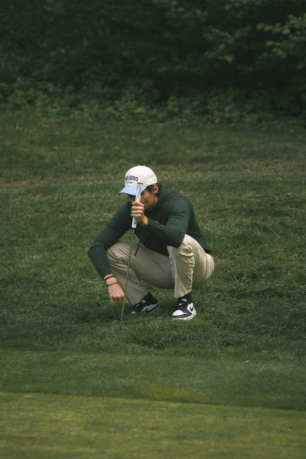 Golfspiller på hug på greenen i beige bukser