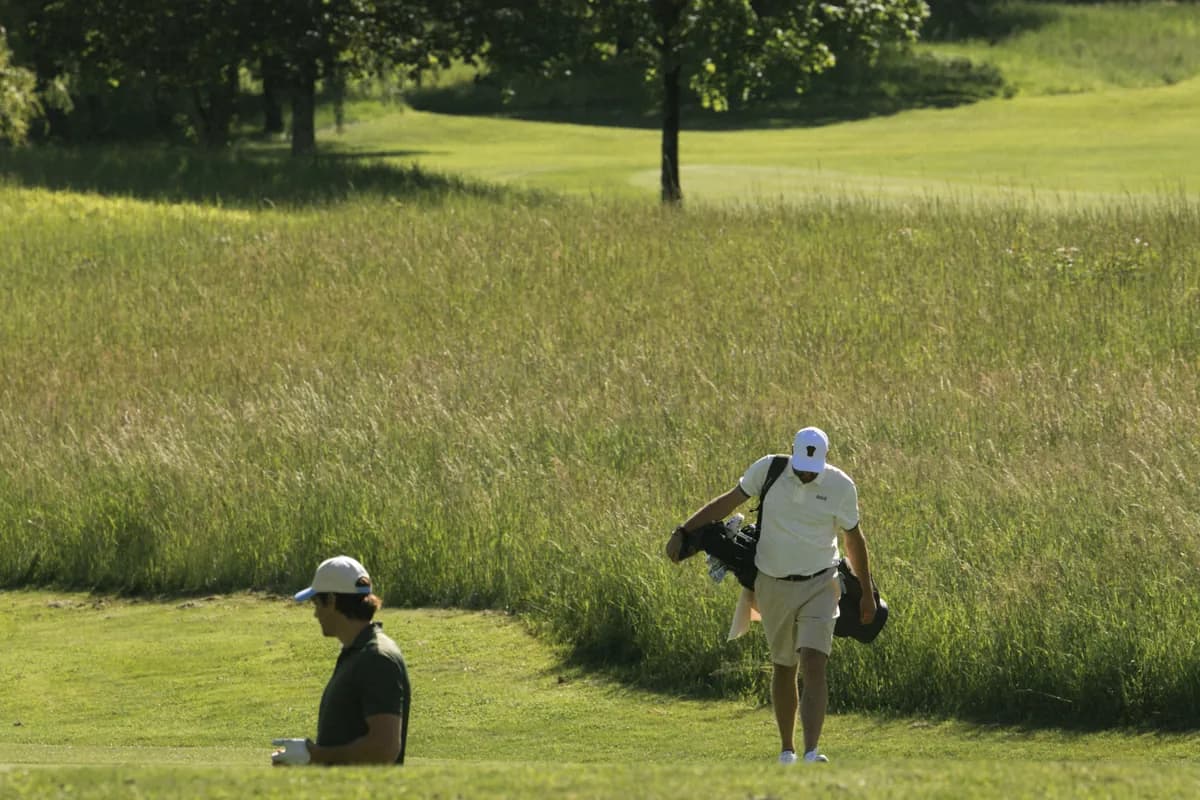 Två golfspelare på ett kort hål kantat av högt gräs